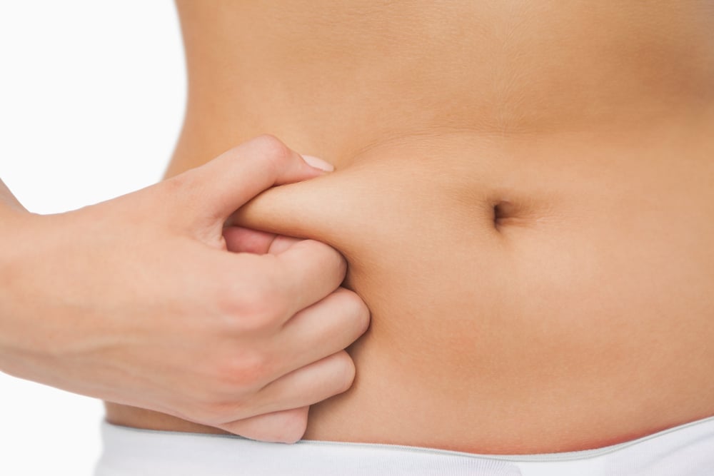 Young slim woman with little fat on her belly on white background